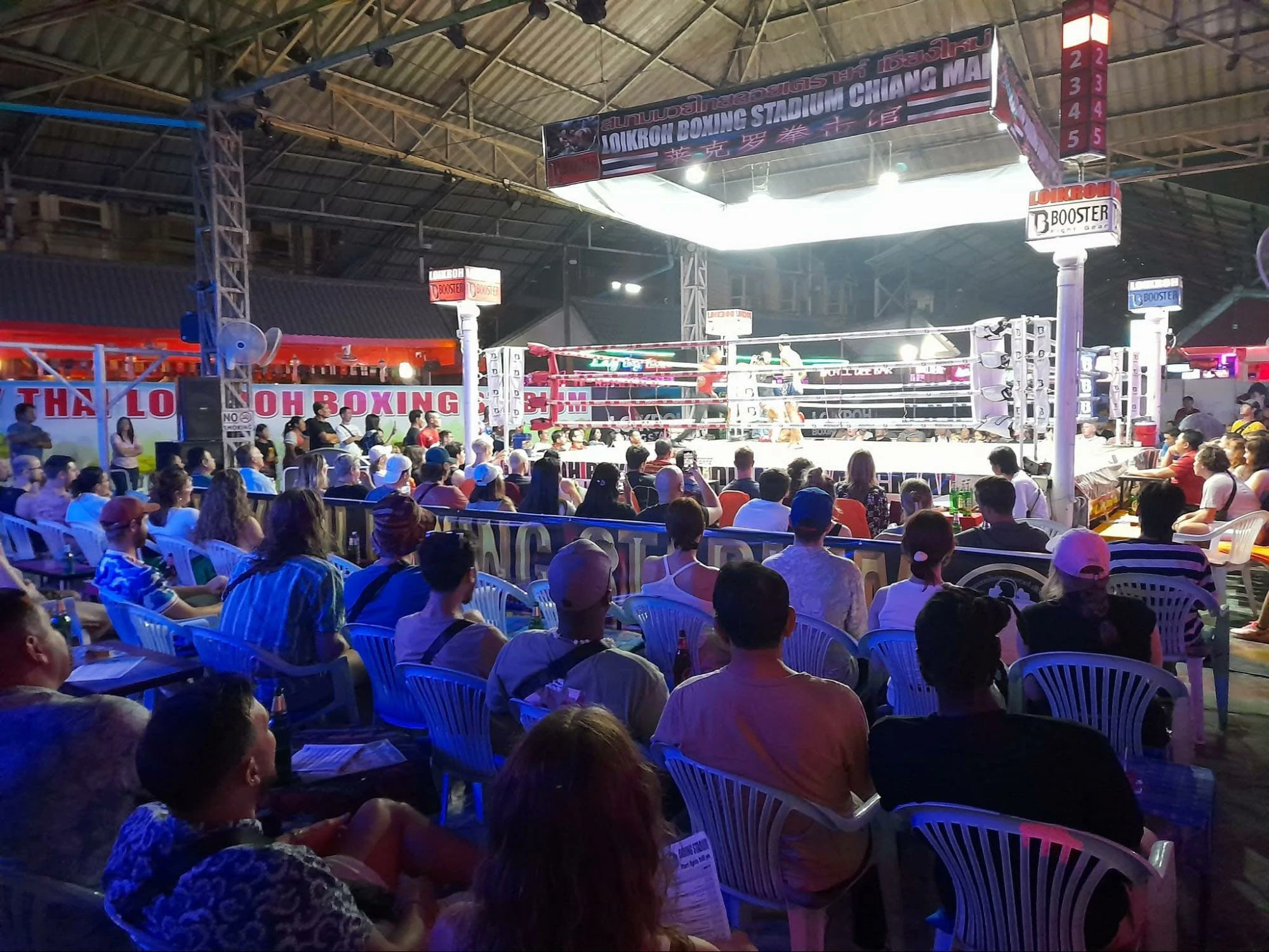 A crowded audience watching a Muay Thai boxing match at Loi Kroh Boxing Stadium in Chiang Mai, with vibrant lighting and an engaged atmosphere.