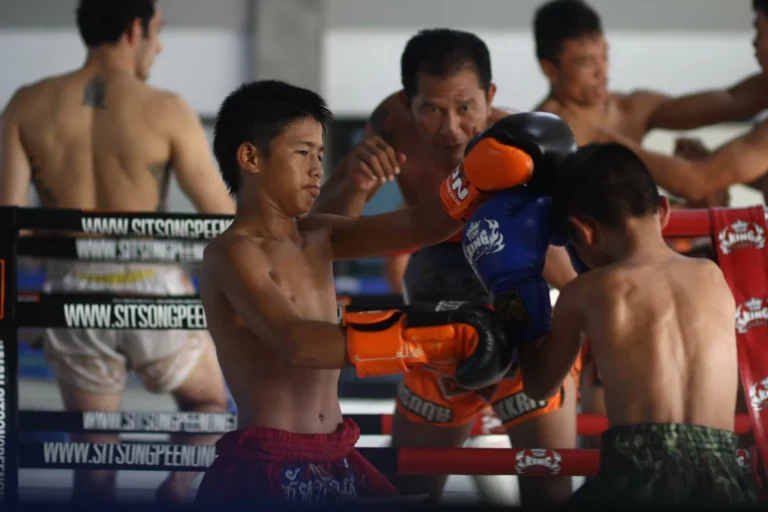 Two young Muay Thai fighters sparring in the ring with trainers supervising, focusing on technique and discipline.